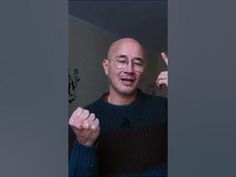 a bald man wearing glasses and pointing to the side with his finger in front of him