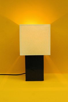 a lamp that is sitting on top of a yellow surface with a black base and a white square light shade