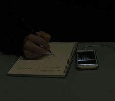 a person writing on a notepad next to a cell phone