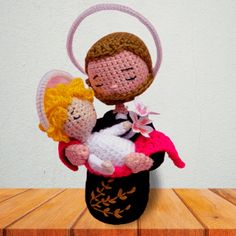 a crocheted doll holding a stuffed animal on top of a wooden table next to a white wall