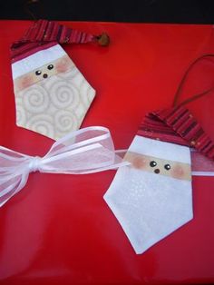 two paper santa claus ornaments on top of a red table with white ribbon around them