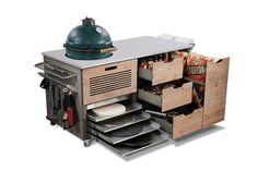 an outdoor grill with drawers and plates in the bottom drawer, next to a large green object