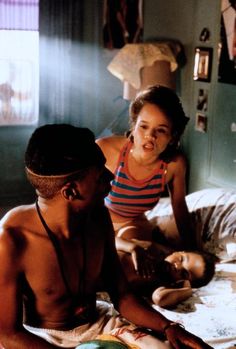 a man sitting on top of a bed next to a woman in a red and white striped shirt