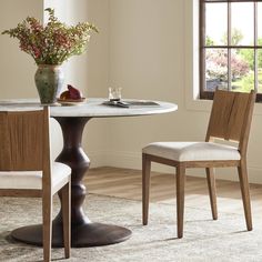 a dining room table with two chairs and a vase full of flowers on the table