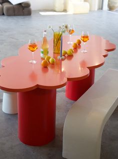 an orange table with wine glasses and bottles on it, next to a white bench