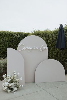 a white sign sitting on top of a sidewalk next to a flower pot and umbrella