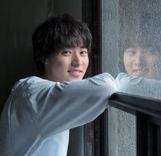 a young man standing next to a window with his arm on the railing looking out