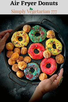 a pan filled with donuts sitting on top of a table next to two hands