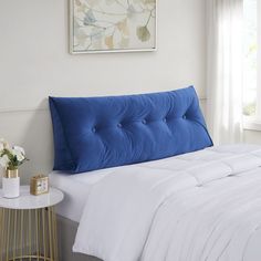 a bed with a blue headboard and white sheets in a room next to a window