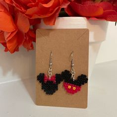 a pair of mickey and minnie mouse earrings on a card with flowers in the background