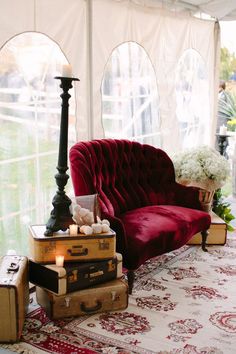 a red velvet couch sitting on top of a rug next to suitcases and a lamp