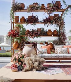 an outdoor seating area with potted plants and flowers on the back wall, along with rugs and pillows