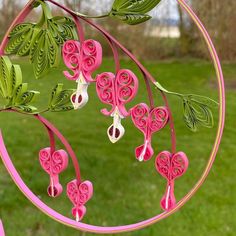 pink paper flowers are hanging from a circular object in the grass with trees behind them