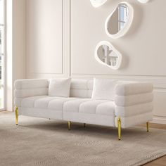 a white couch sitting on top of a wooden floor next to a wall mounted mirror