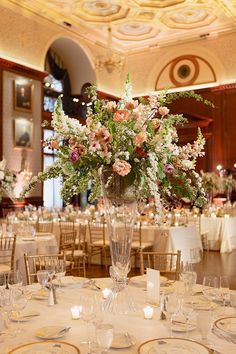 an elegant centerpiece is displayed in the middle of a banquet room with white linens and gold chargers