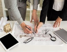 three people are working on architectural drawings at a table