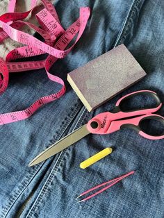 pink scissors, measuring tape, and other items laid out on a jean jacket with the jeans rolled down