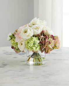 a vase filled with white and pink flowers on top of a marble table next to a window