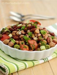 a white bowl filled with bean salad on top of a green and white striped napkin