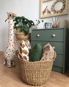 two stuffed giraffes sitting next to each other near a basket filled with pillows