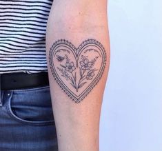 a woman's arm with a heart shaped tattoo and flowers on the inside of it