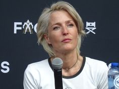 a woman sitting at a table with a microphone in front of her and a bottle of water behind her