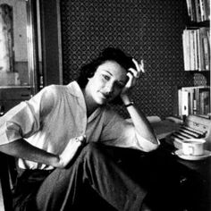 a woman sitting at a desk with her hand on her head and an old typewriter in the background