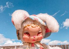 a close up of a toy doll wearing a hat and holding something in her hand