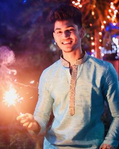 a man in a blue shirt and tie holding a sparkler with lights behind him