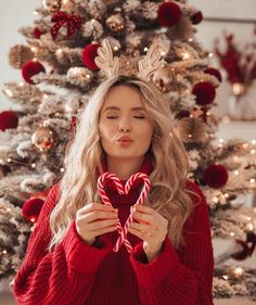 a woman holding a heart shaped lollipop in front of a christmas tree