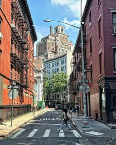 people crossing the street in an urban area with tall buildings on either side and one person walking down the street