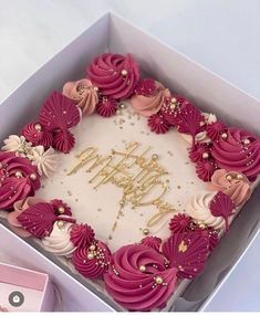 a birthday cake in a box with pink frosting and gold decorations on it's side