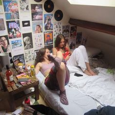 two women sitting on a bed in a dorm room with posters all over the wall