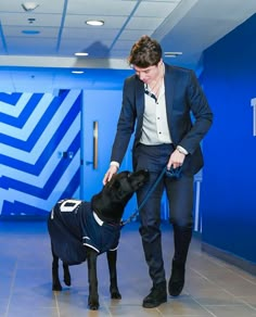 a man in a suit and tie is petting a black dog wearing a sweater