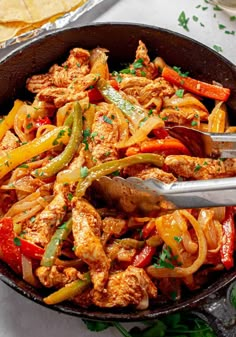 a skillet filled with chicken and peppers next to tortilla chips on a table