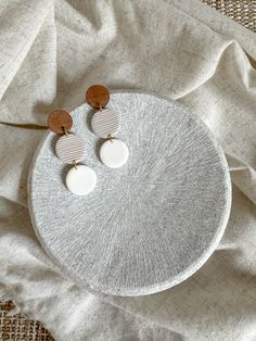 two white and brown earrings sitting on top of a cloth covered table next to a piece of fabric