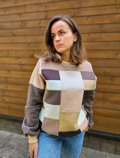 a woman standing in front of a wooden wall wearing a brown and tan striped sweater