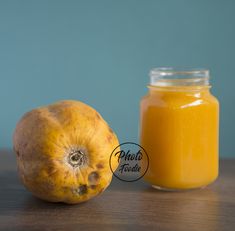 a glass jar filled with orange juice next to an unpeeled pumpkin on a wooden table