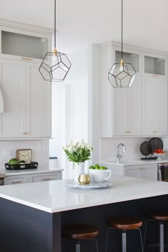 a kitchen island with three hanging lights and two vases filled with flowers on it