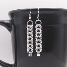 two pairs of silver earrings sitting on top of a black coffee cup in front of a mug