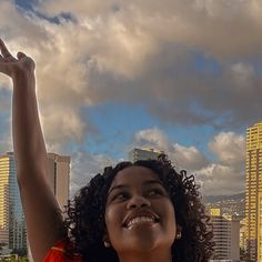 a woman is smiling and waving in front of the city skyline with her hand up