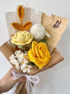 a hand holding a bouquet of flowers made out of crocheted yarn and paper