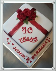 a white cake with red ribbon and roses on it that says 40 years john & barbara