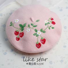 a pink hat with strawberries and daisies embroidered on the front, sitting on a table