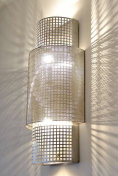 a wall mounted light fixture on the side of a white wall with shadows coming through it