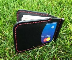 a black wallet with red stitching on the front and side, sitting in grass