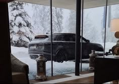 a car is parked in front of a large window with snow on the ground and trees outside