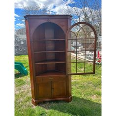 an old wooden bookcase with arched glass doors on the top and bottom shelf is sitting in grass