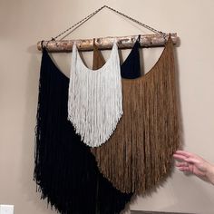 three different colored fringes hanging from a wooden frame on a wall next to a person's hand