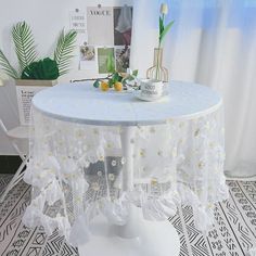 a white table with flowers on it in front of a potted plant and window